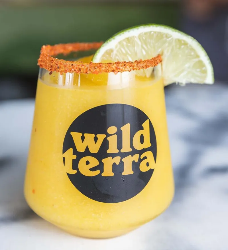 Frozen mango margarita with a chili-spiced rim and lime wedge in a branded glass