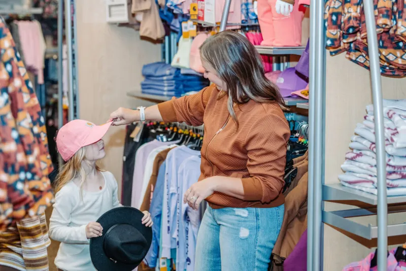 Woman placing a pink baseball cap on a young girl in a clothing store