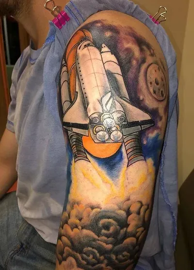 Space shuttle launch tattoo sleeve on a person's upper arm with cosmic nebula background
