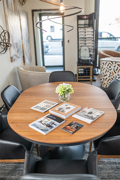 Round wood table with design catalogs and small floral centerpiece in a bright interior design studio showroom