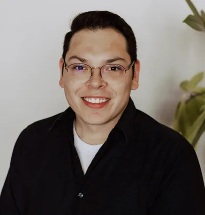 Smiling young man with glasses and black shirt against a light background