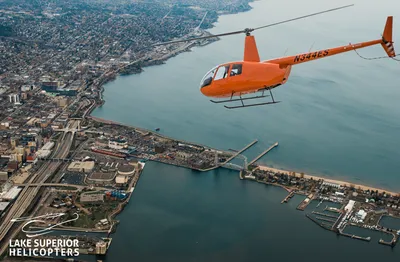 Orange helicopter flying over a coastal city and harbor from an aerial view