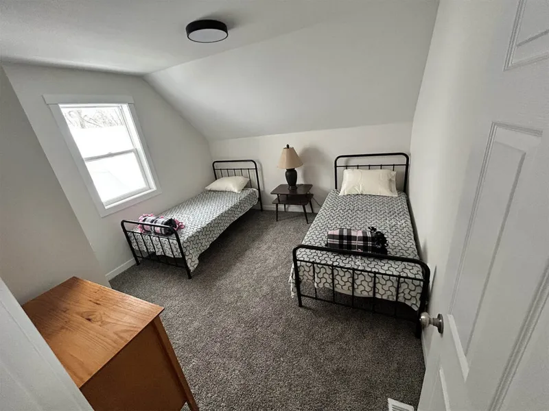 Attic bedroom with two black metal twin beds, patterned duvets, and a small nightstand