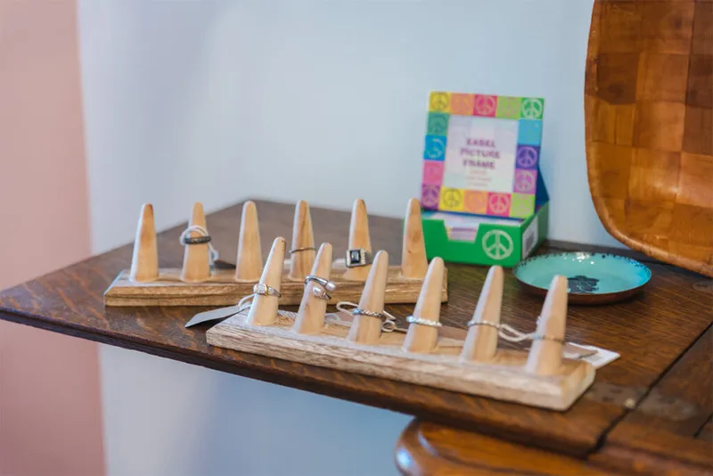 Wooden ring display stands holding assorted rings on a dark wood table beside a colorful peace-sign picture frame box