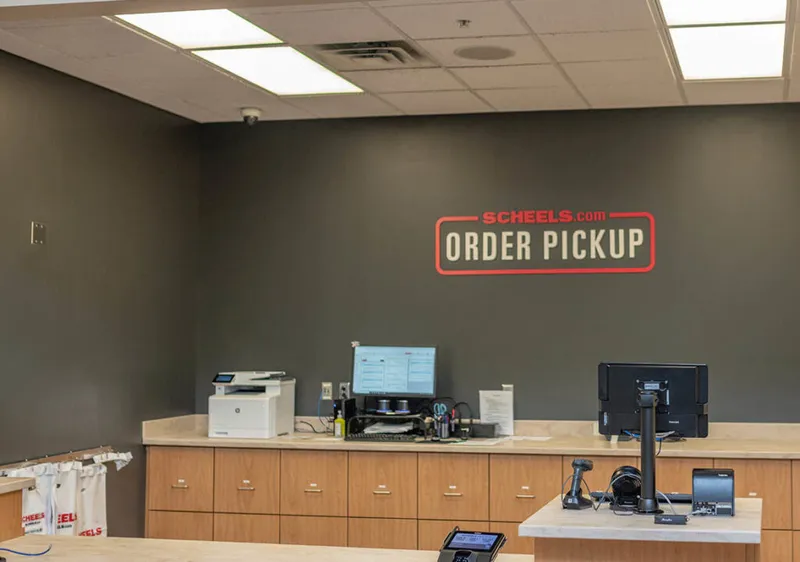 Scheels.com Order Pickup counter with wood cabinets, monitors, and a printer