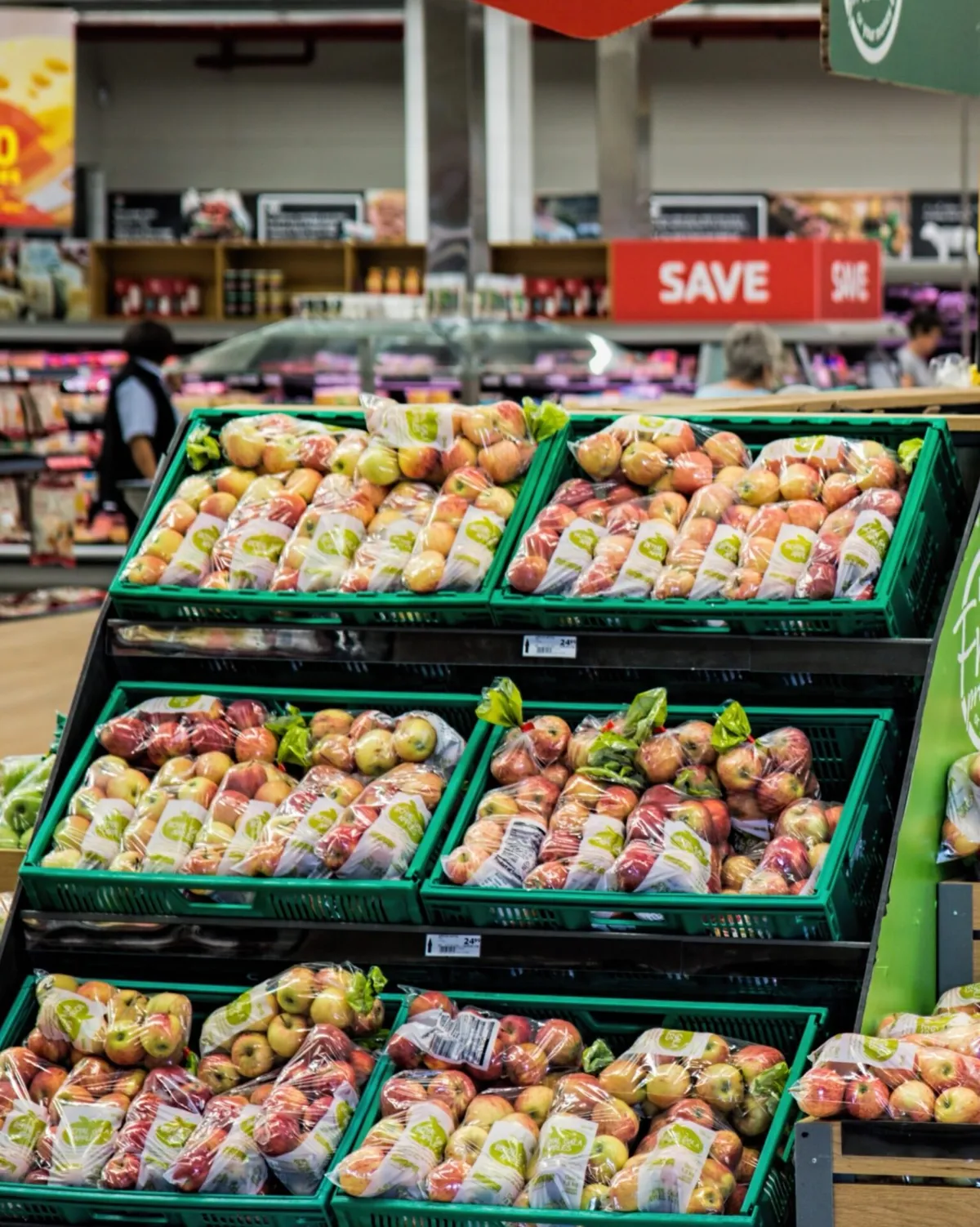 Bagged apples stacked in green crates on a tiered supermarket produce display