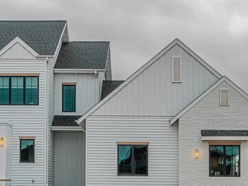 White farmhouse-style home exterior with board-and-batten siding, black windows, and gray shingle roofline under overcast sky