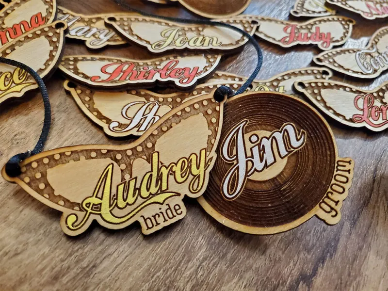Laser-engraved wooden name tags labeled bride and groom among others on a wood surface