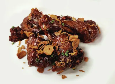 Glazed chicken wings topped with crispy fried garlic and chopped scallions on a white plate