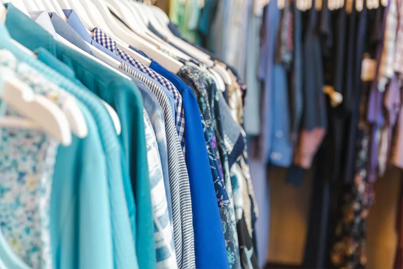 Rows of blue and teal women's clothing hanging on white hangers in a boutique