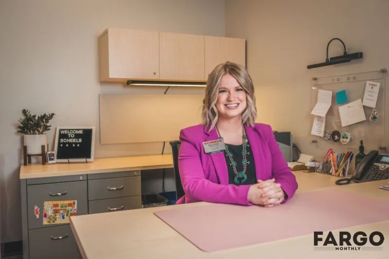 Smiling woman in a magenta blazer seated at a desk in a corporate office