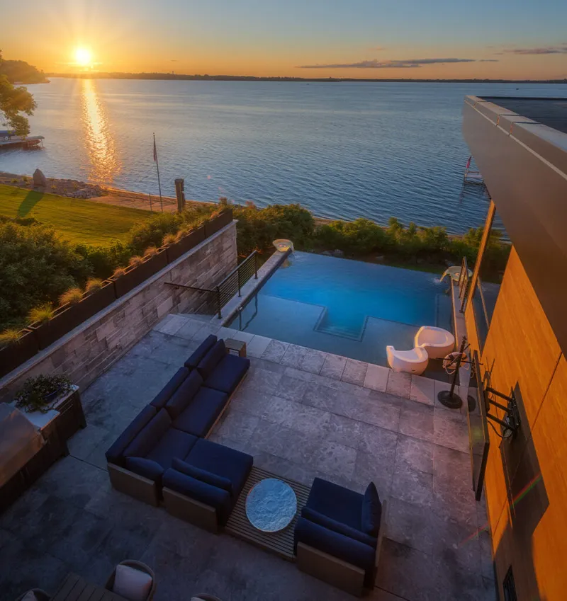 Aerial view of a lakeside patio with navy sectional seating and infinity pool at sunset