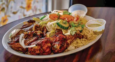 Platter of grilled chicken with rice, fresh salad, and dipping sauces
