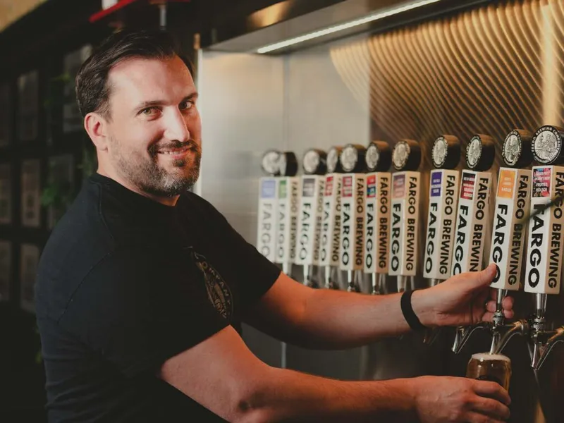 Smiling bartender pulling a draft beer at a row of Fargo Brewing tap handles
