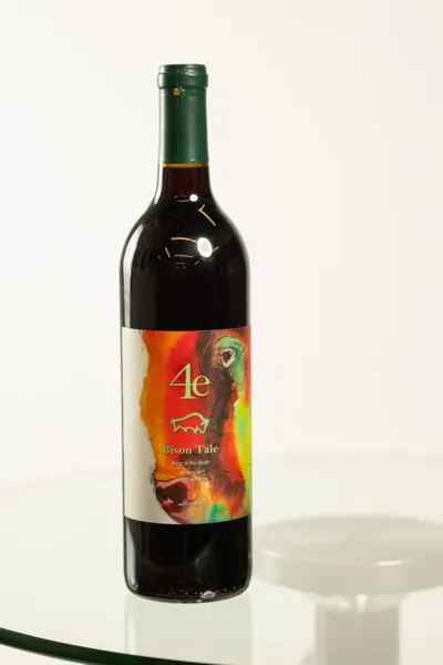 Bottle of 4e Bison Tale red wine with colorful painted label on a glass surface