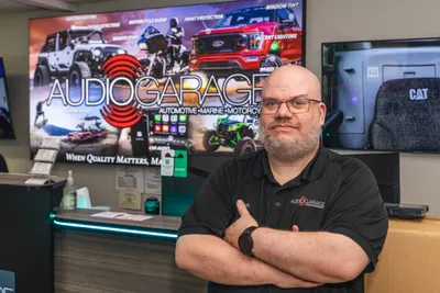 Man with arms crossed standing in front of an Audio Garage branded display screen