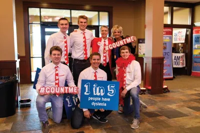 Group of seven people in red ties and scarves holding '1 in 5 people have dyslexia' and #COUNTME signs