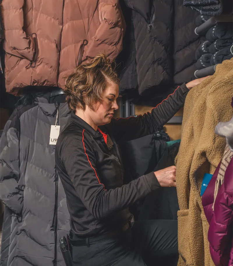 Woman in black uniform browses a rack of puffy winter coats in a sporting goods store
