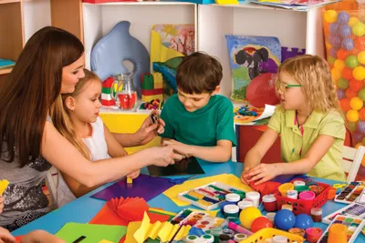 Adult and three children doing crafts at a colorful table full of art supplies
