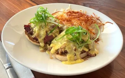 Eggs Benedict with hollandaise, shredded green onion, and a crispy hash brown on a white plate