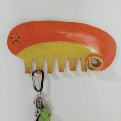 Orange and yellow ceramic wall hook shaped like an angry cartoon creature, holding keys