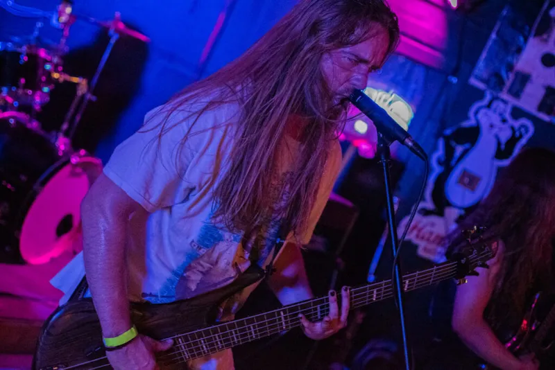 Long-haired guitarist leans into a microphone under purple and blue stage lights