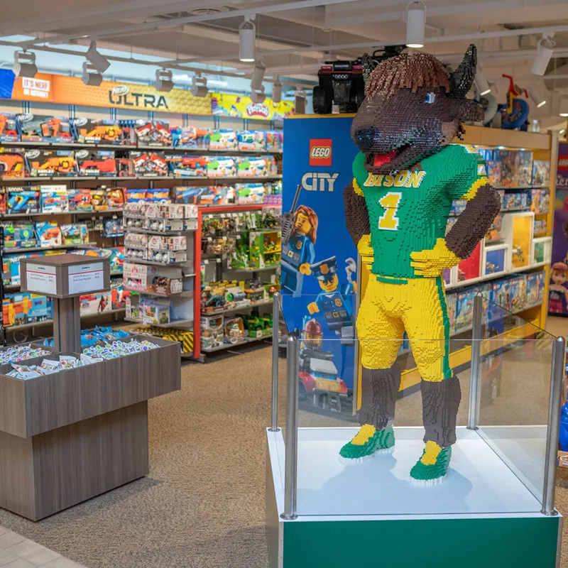 Life-size LEGO bison mascot in a green-and-yellow football uniform displayed in a toy store