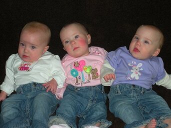 Three infants in jeans and colorful tops seated side by side