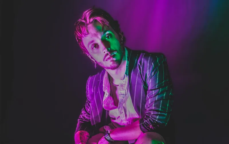 Young man in a pinstripe blazer posed under vibrant purple and green stage lighting