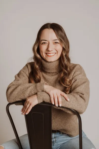 Smiling woman in a tan turtleneck sweater leaning on the back of a metal chair