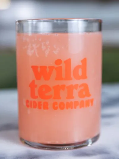 Glass of pink cider with Wild Terra Cider Company branding