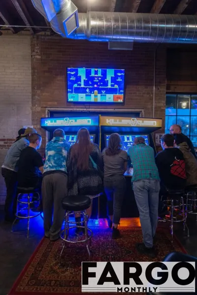 Group of people playing a large Killer Queen arcade cabinet in a brick-walled bar
