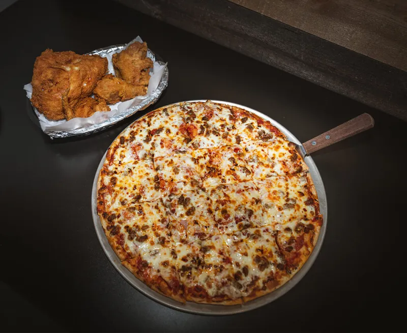 Whole cheese and meat pizza on a metal pan beside fried chicken wings in a foil tray