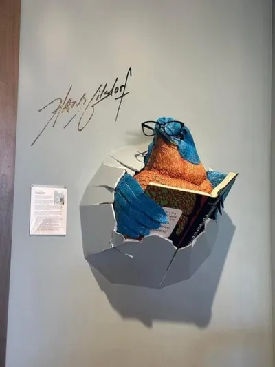 3D wall sculpture of a colorful bird wearing glasses and reading a book, bursting through a wall