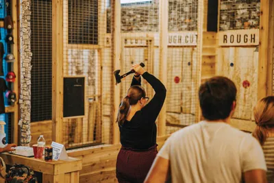 Woman raising an axe overhead at an indoor axe-throwing venue