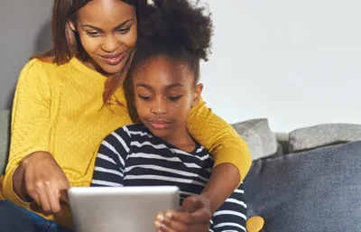 Woman in yellow sweater and girl looking at a tablet together on a couch