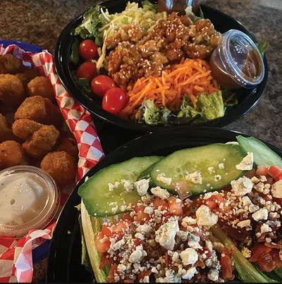 Two salads and a basket of fried appetizers on a granite counter
