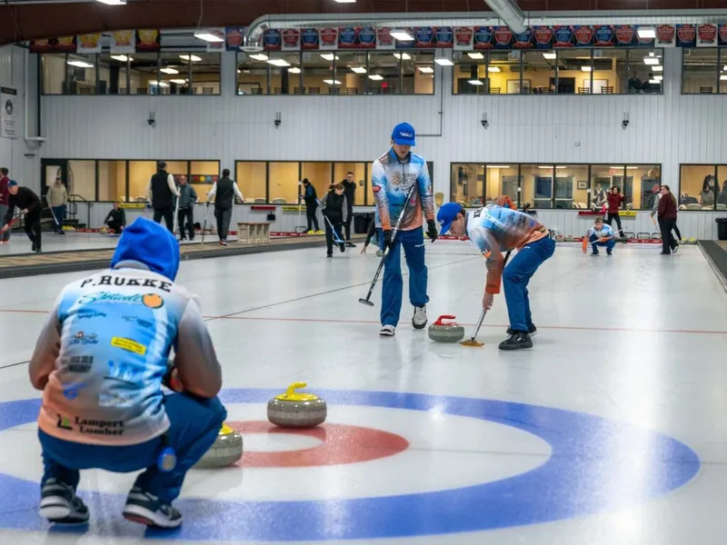 Curling players sweep and watch stones on an indoor ice sheet during a match