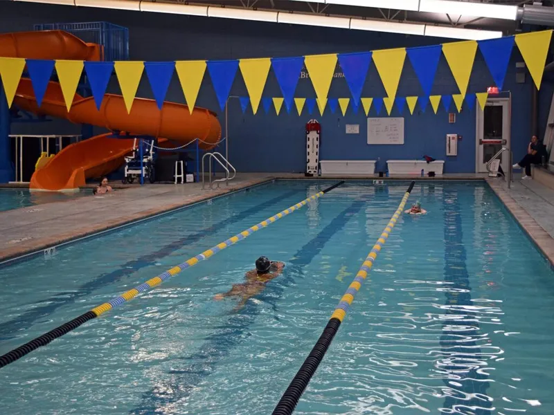 Swimmers in lane lines at an indoor pool with an orange water slide and blue-and-yellow pennant flags