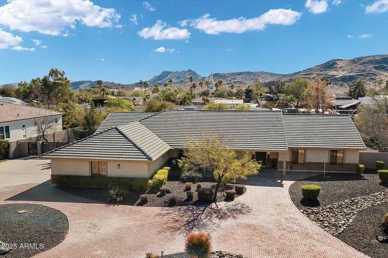 Single-story ranch home with tile roof, paver driveway, and desert landscaping backed by mountain views