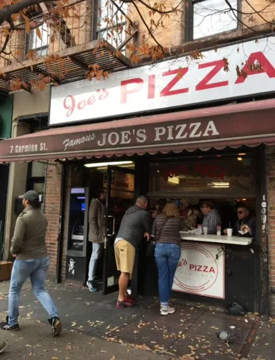 Customers ordering at the walk-up window of Joe's Pizza on Carmine St