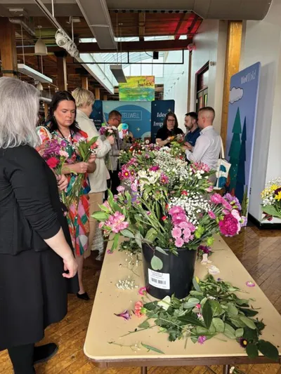 People arranging colorful mixed flowers at a long table during an indoor community event