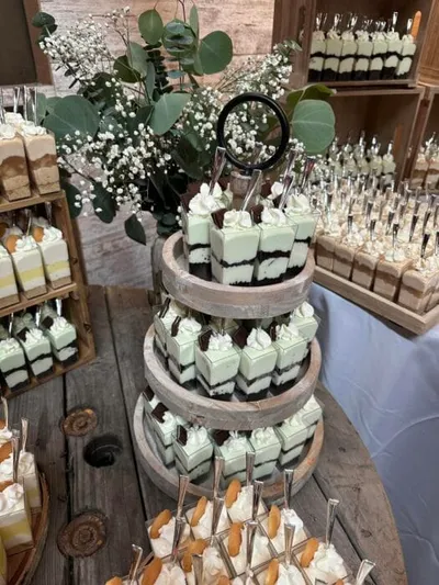 Three-tier rustic wooden stand holding mint-topped chocolate dessert cups, surrounded by floral greenery and additional