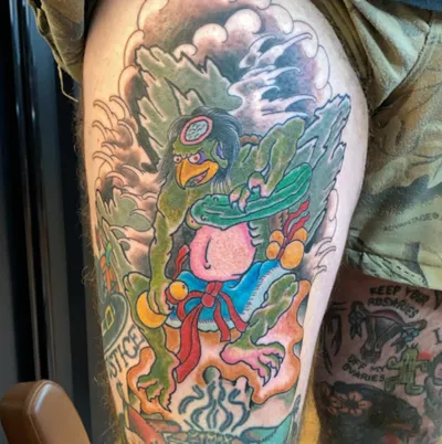 Colorful traditional-style tattoo of a green bird deity with red sash on a person's upper arm