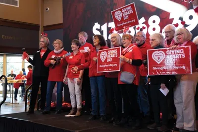 Group of volunteers in red shirts holding Giving Hearts Day signs on a stage