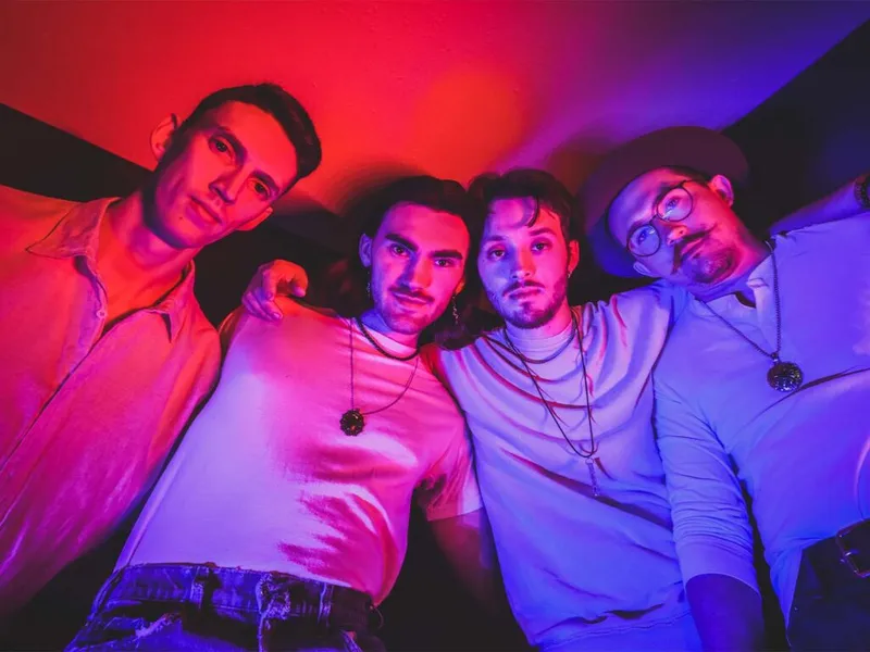 Four young men posing together under red and purple stage lighting