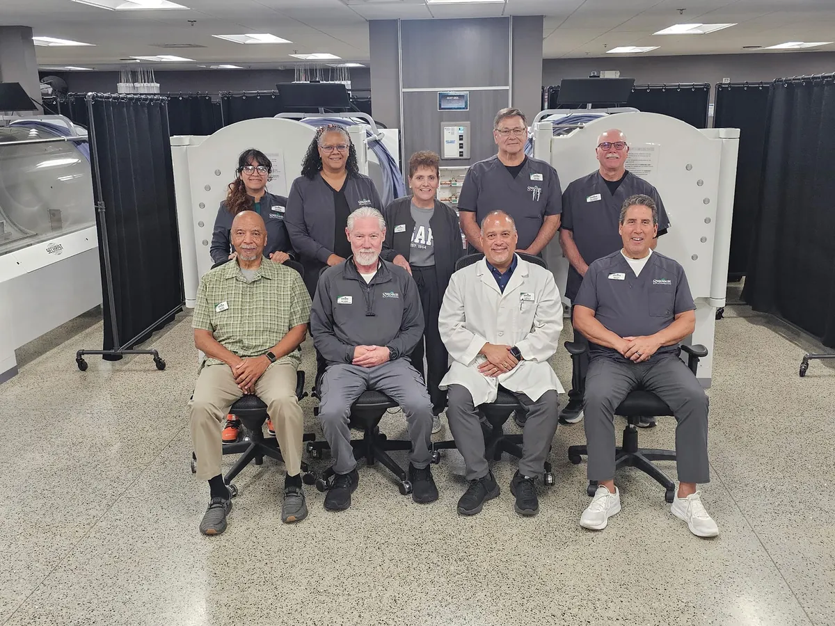 Nine medical staff members posing in a clinical room with hyperbaric chambers