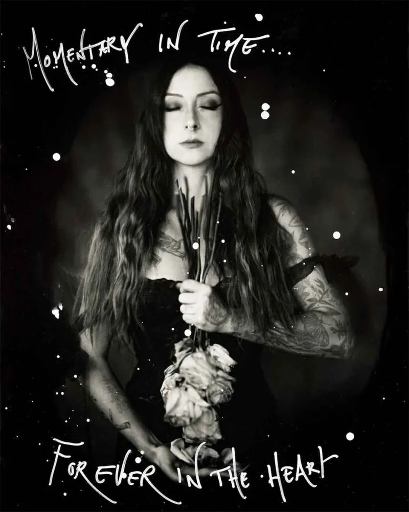 Black-and-white wet plate portrait of a tattooed woman with long dark hair holding wilted roses, eyes closed