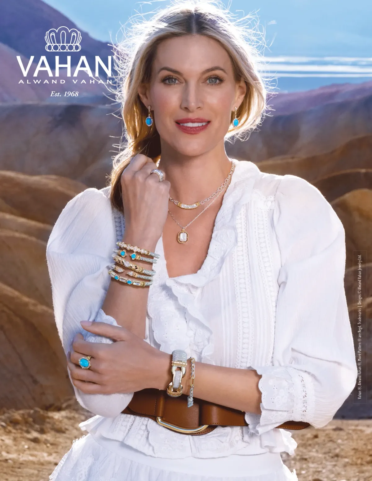 Woman in white eyelet blouse wearing layered gold necklaces, stacked bracelets, and turquoise earrings against a desert