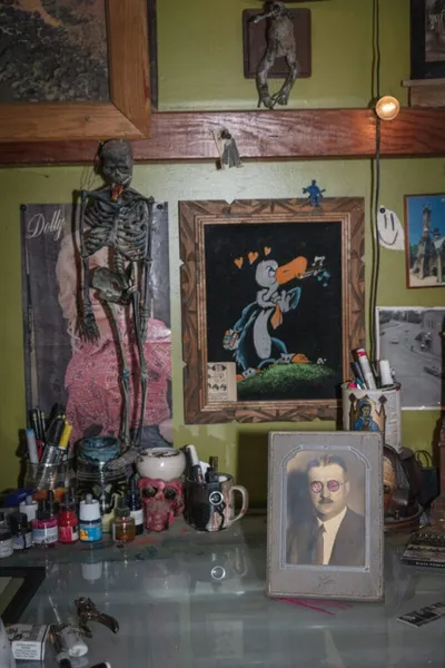 Cluttered artist's desk with a skeleton figure, cartoon artwork, vintage portrait, and art supplies